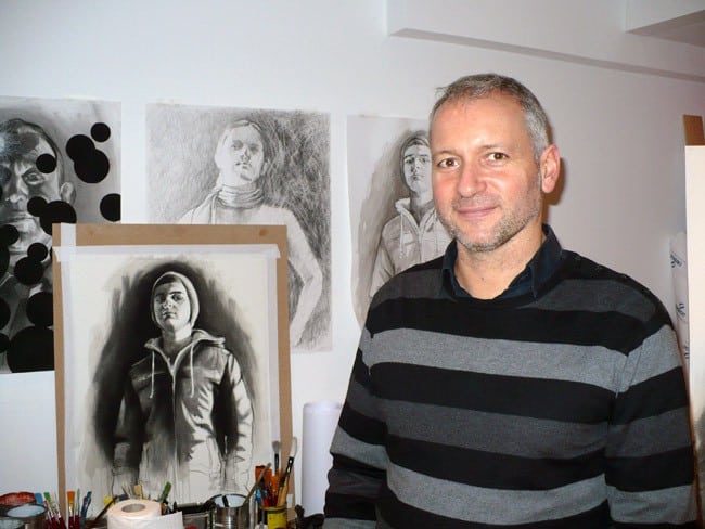 Fabrice Nesta artiste plasticien cogérant de l'Atelier Bis rue Saint Laurent à Grenoble souriant devant des portraits dessinés en noir et blanc © Delphine Chappaz - placegrenet.fr