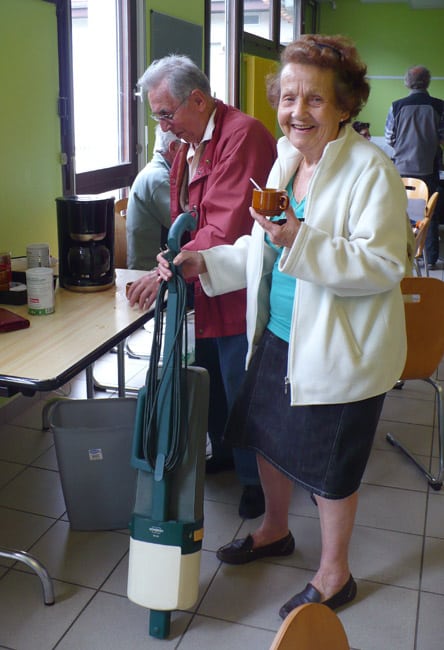 Vieille dame avec son aspirateur balai réparée au Répair Café de Saint-Egrève avec une tasse de café dans la main Crédit photo Delphine Chappaz