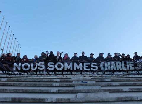 Banderole Nous sommes Charlie Nous sommes tous Ahmed, Bernard, Elsa, Cabu, Charb, Franck… déployée sur les gradins de l'anneau de vitesse de Grenoble lors de la marche républicaine © Maïlys Medjadj – placegrenet.fr