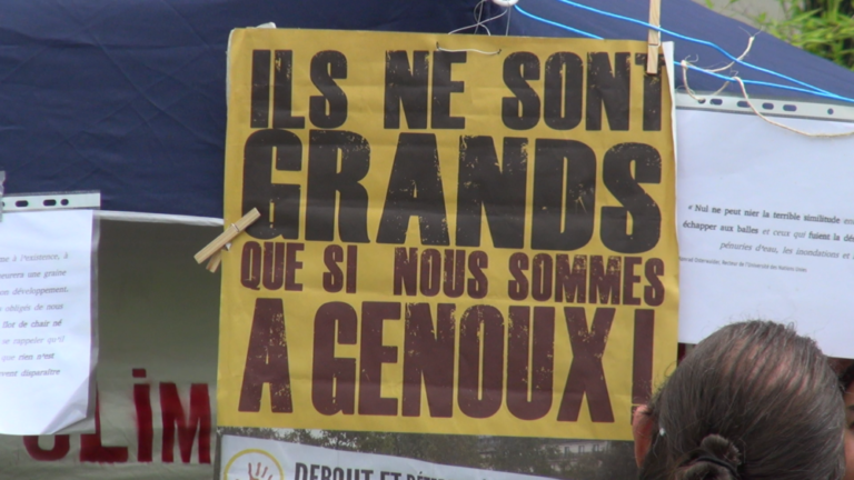 Pancarte "Ils ne sont grands que si nous sommes à genoux" pendant un rassemblement devant le tribunal de Grenoble le 30 juin 2021(c) Ilan Khalifa--Delclos | Place Gre'net