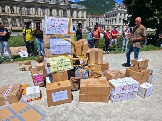 À l'appel de la coordination Bouge ta pref, une pyramide matérialisant symboliquement le nombre de dossiers de titres de séjour en attente a été érigée, mercredi 10 juin 2026 devant la préfecture de l'Isère. © Joël Kermabon - Place Gre'net